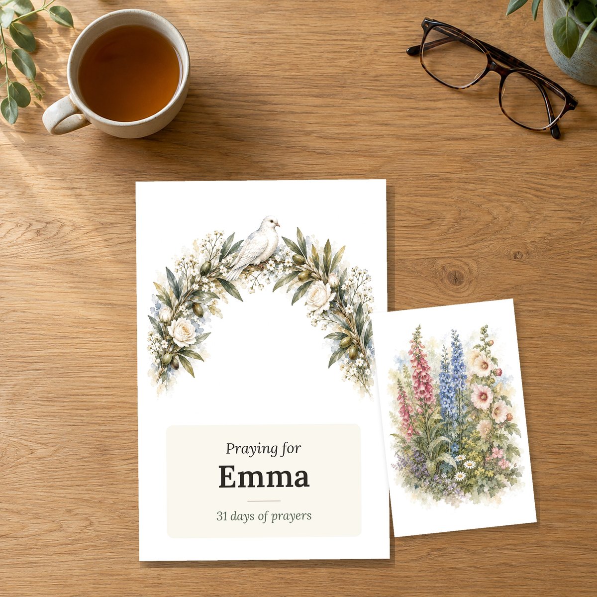 The Praying for Emma box front beside a card with a watercolor-style flower illustration, on an oak table
